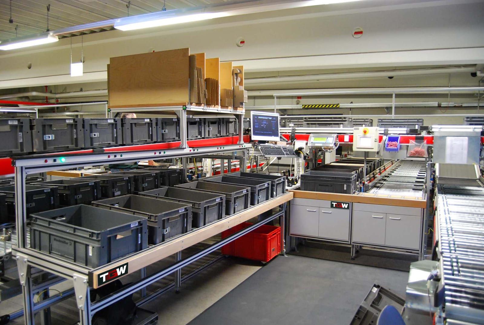 A screen and keyboard built into a warehouse picking station, surrounded by empty totes and roller conveyor.